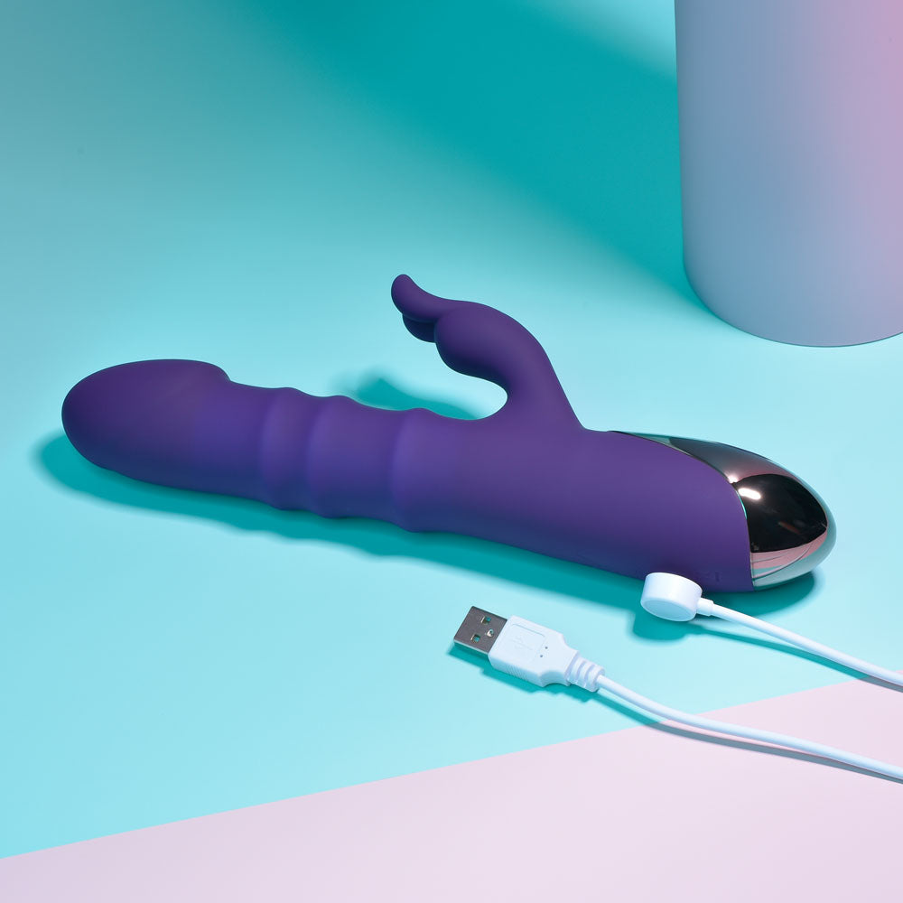 Purple electronic device with USB cable on a teal and pink background