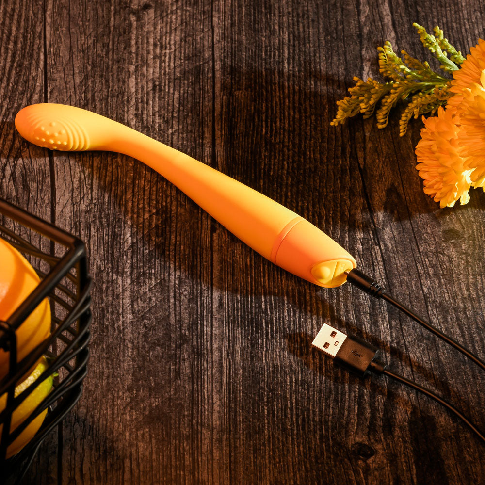 Orange electronic device with USB cable on a wooden surface with flowers.