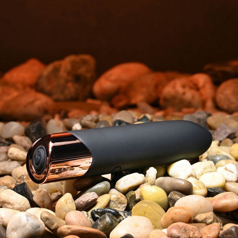 Black and gold camera on pebbles with a warm-toned background