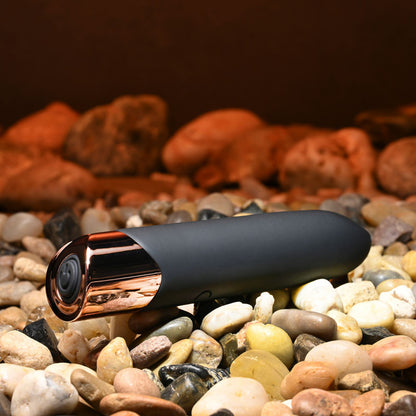 Black and gold camera on pebbles with a warm-toned background