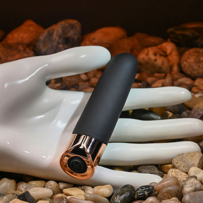 Black and rose gold electronic device held by a white ceramic hand against a rocky background