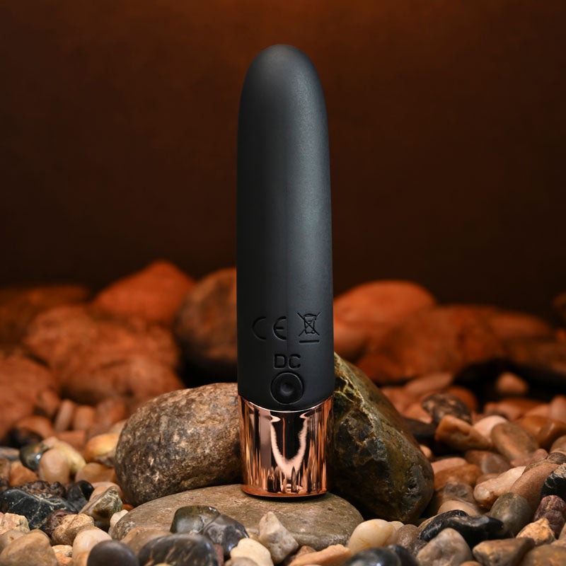Black and rose gold device on a bed of rocks with a dark brown background