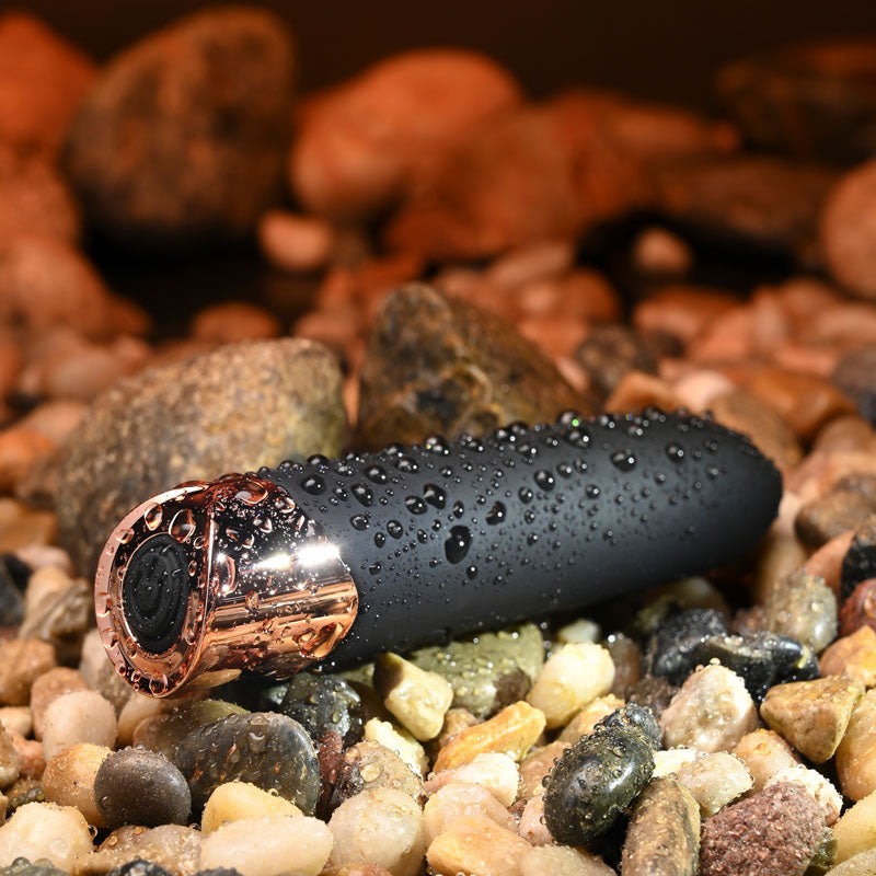 Black and rose gold object with water droplets on pebbles