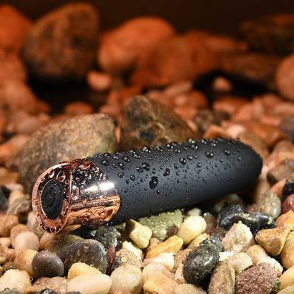 Black and rose gold object with water droplets on pebbles