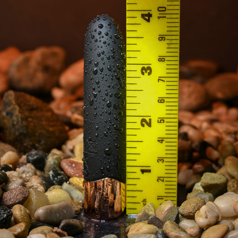 Black cylindrical object with water droplets on a yellow measuring tape against a rocky background
