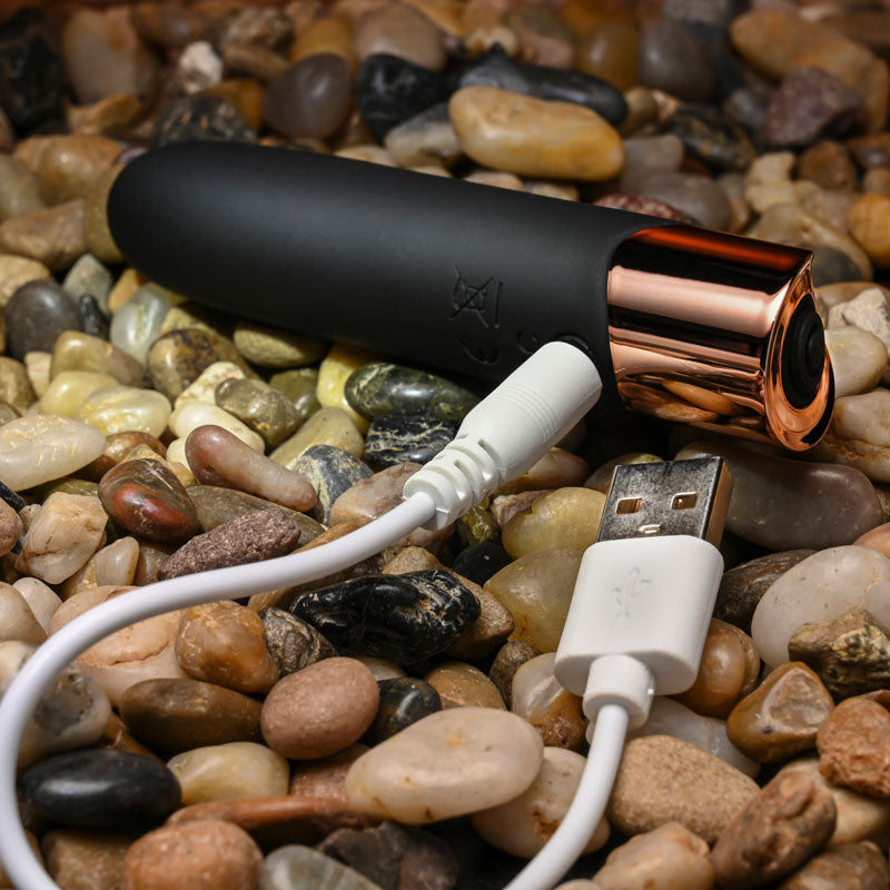 Black and rose gold electronic device with white cable on pebbles