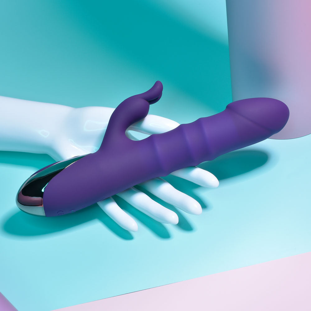 Purple and silver handheld massager on a white hand against a teal background