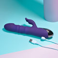 Purple electronic device with USB cable on a teal and pink background