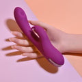 Hand holding a purple electronic device against a pink and orange background
