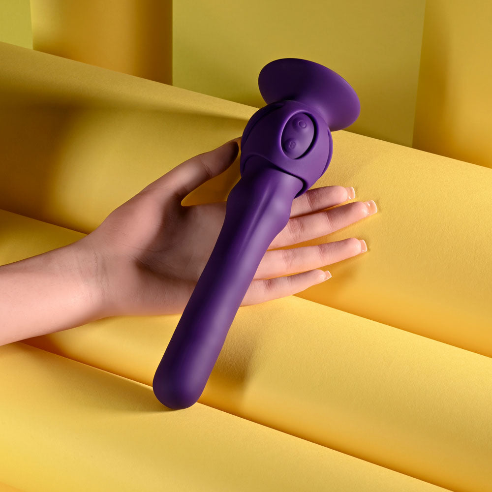 Purple handheld massager held by a hand on a yellow background