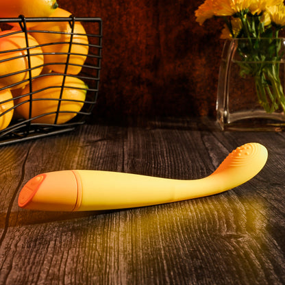 Yellow and orange object on a wooden surface with a basket of oranges and flowers in the background.