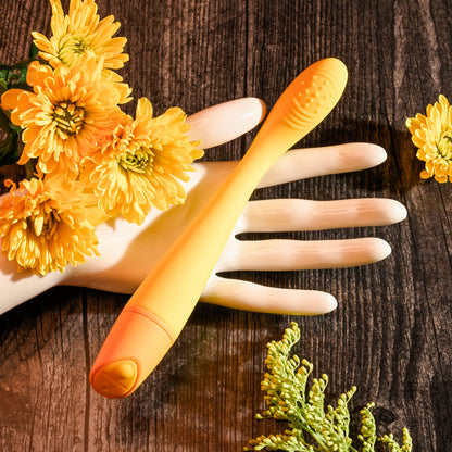 Orange electronic device held by a hand with yellow flowers on a wooden surface