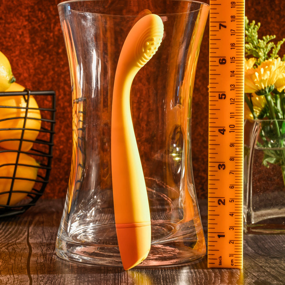 Yellow and orange object resembling a spoon or tool inside a clear glass container with a ruler for scale on a wooden surface.