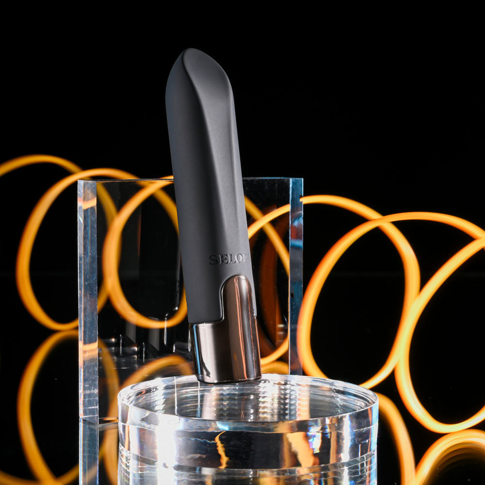 Black wine bottle stopper with silver base on a clear stand against a black background with orange circular lights.