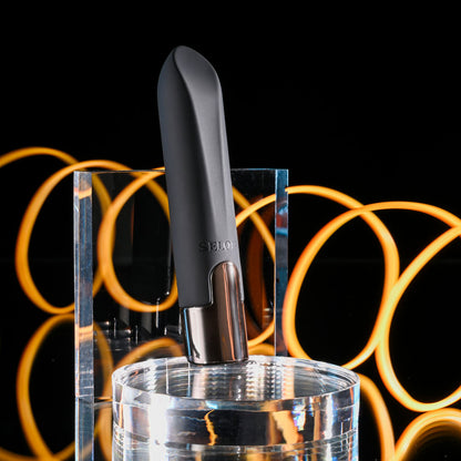 Black wine bottle stopper with silver base on a clear stand against a black background with orange circular lights.