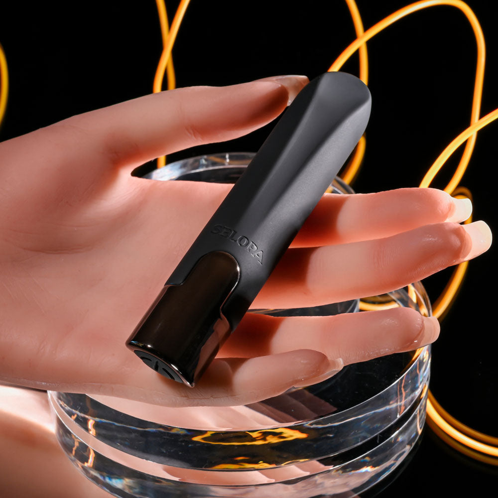Hand holding a black vape device over a glass with a dark background and glowing orange elements.