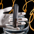 Black and silver device held by a white hand on a clear stand with neon lights in the background