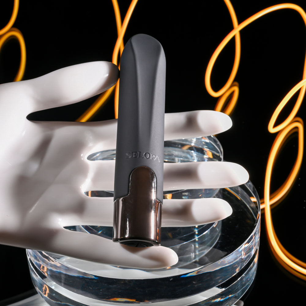 Black and silver device held by a white hand on a clear stand with neon lights in the background
